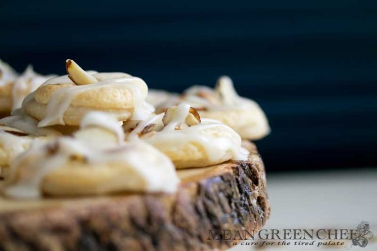 Almond Pastry Cookies on white wooden background with roasted almonds sprinkled around.