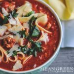 Overhead photo of Lasagna Soup garnished with fresh basil and homemade egg noodles with a scalloped spoon on a gray background.