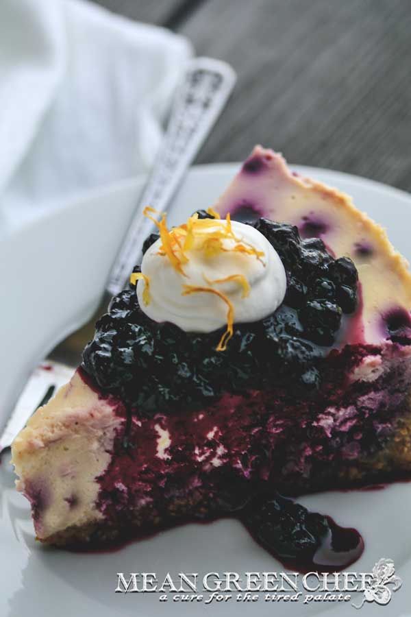 Side photo of a slice of Blueberry Lemon Cheesecake topped with blueberries and fresh whipped cream.