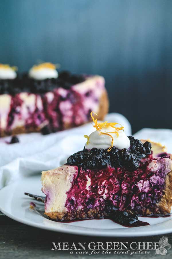 Side photo of a slice of Blueberry Lemon Cheesecake topped with blueberries and fresh whipped cream.