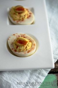 Classic Deviled Eggs on a large with platter with circle and square depressions for the eggs, sitting on a white cotton kitchen towel on an old blue wooden background. Mean Green Chef