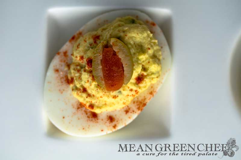 Classic Deviled Eggs on a large with platter with circle and square depressions for the eggs, sitting on a white cotton kitchen towel on an old blue wooden background. Mean Green Chef