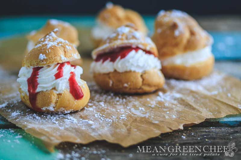 Cream Puffs with Strawberry Coulis shown with a sprinkling of powdered sugar on an old blue wooden background