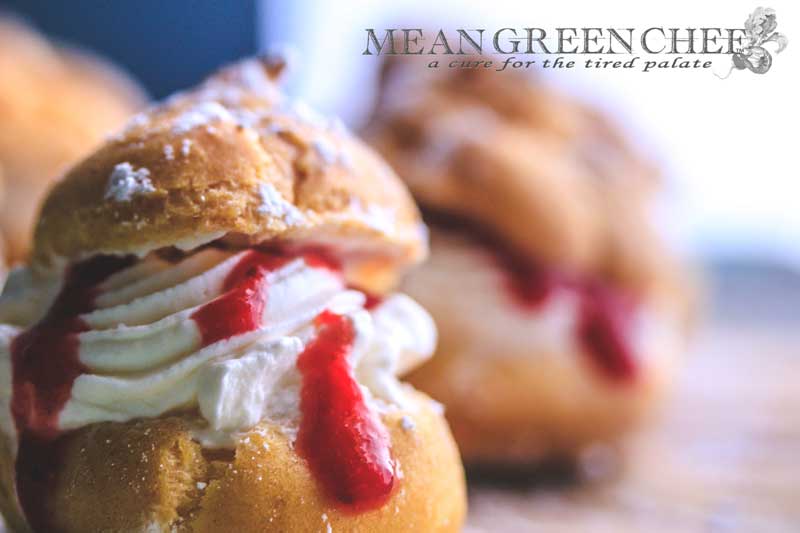 Cream Puffs with Strawberry Coulis shown with a sprinkling of powdered sugar on an old blue wooden background