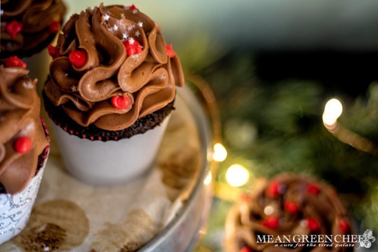 Side photo of Bakery Style Chocolate Cupcake decorated with a high swirl of chocolate frosting red frosting berries and a sprinkle of silver stars in a scalloped gray cupcake wrapper.