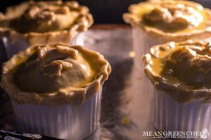 Side photo of double crust chicken pot pies in white ramekins baking in the oven.