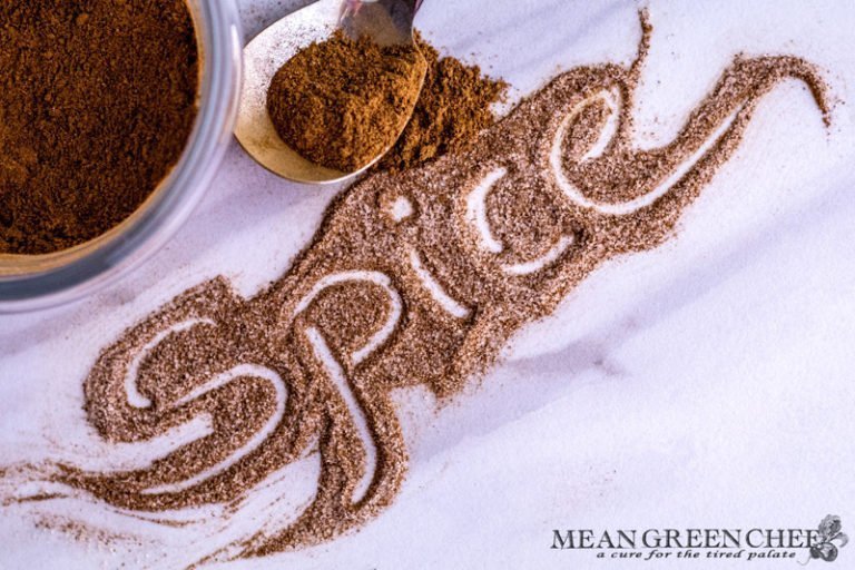 Apple Pie Spice used to spell out Spice in a fancy swirled font, with a small glass bowl and silver spoon each containing some spice. Mean Green Chef