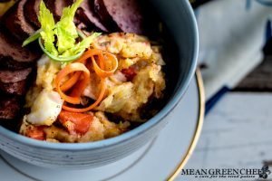 Overhead photo of a bowl of Dutch Stamppot with smoked sausage garnished with carrots and celery sprouts. Mean Green Chef