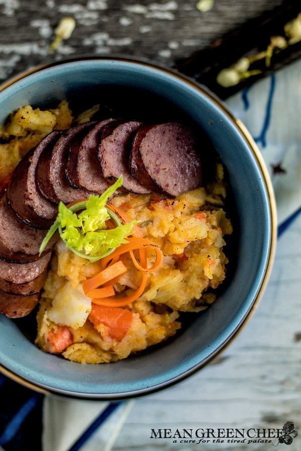 Overhead photo of a bowl of Dutch Stamppot with smoked sausage garnished with carrots and celery sprouts. Mean Green Chef