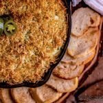 Overhead photo of Jalapeno Popper Dip in a cast iron pan surrounded with toasted sourdough bread rounds. on a rustic wooden background. Mean Green Chef