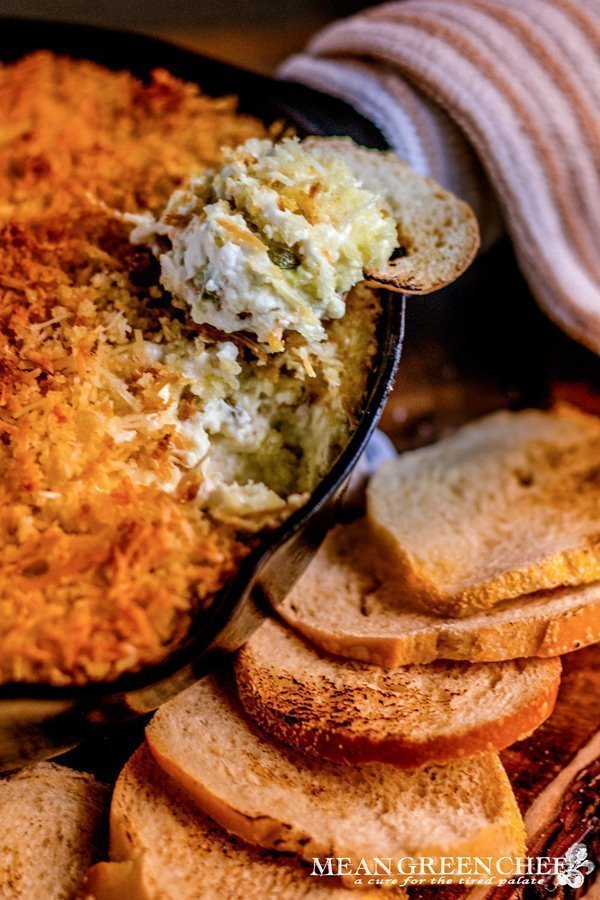Overhead photo of Jalapeno Popper Dip in a cast iron pan surrounded with toasted sourdough bread rounds. on a rustic wooden background. Mean Green Chef