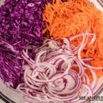Ingredients for Red Cabbage and Carrot Slaw sliced in a large glass bowl on a white marble counter top background. Mean Green Chef