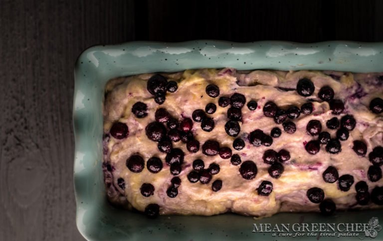 Overhead photo of Rustic Blueberry Banana Bread batter in a blue scalloped loaf pan on a gray wooden background. Mean Green Chef