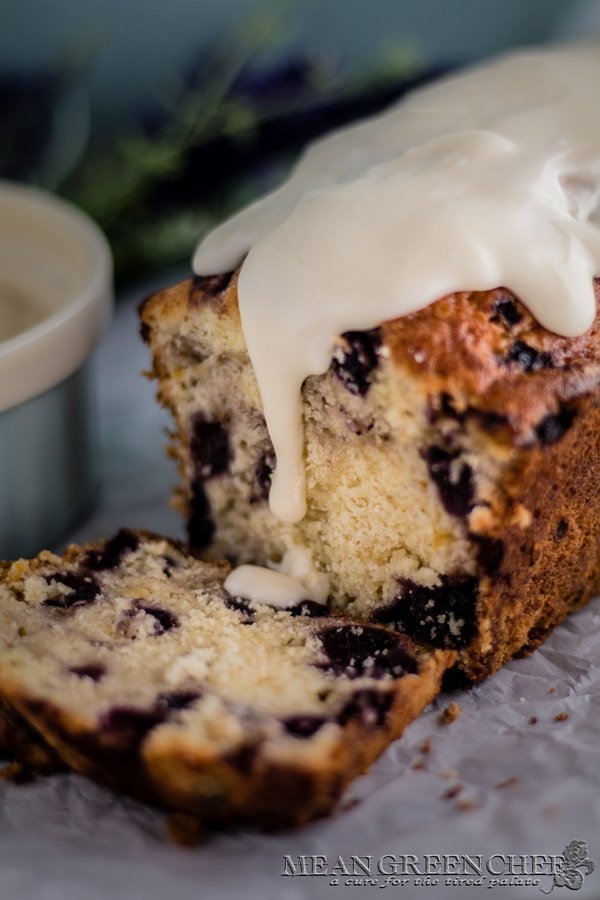 Side photo of Rustic Blueberry Banana Bread with a lush vanilla glaze dripping down a freshly sliced loaf. Mean Green Chef