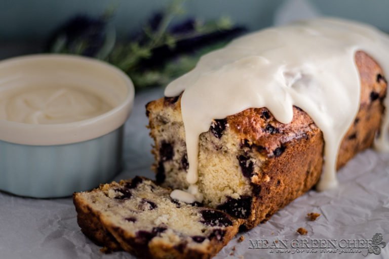 Side photo of Rustic Blueberry Banana Bread with a lush vanilla glaze dripping down a freshly sliced loaf. Mean Green Chef