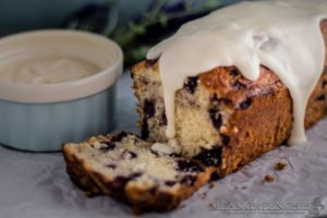 Side photo of Rustic Blueberry Banana Bread with a lush vanilla glaze dripping down a freshly sliced loaf. Mean Green Chef