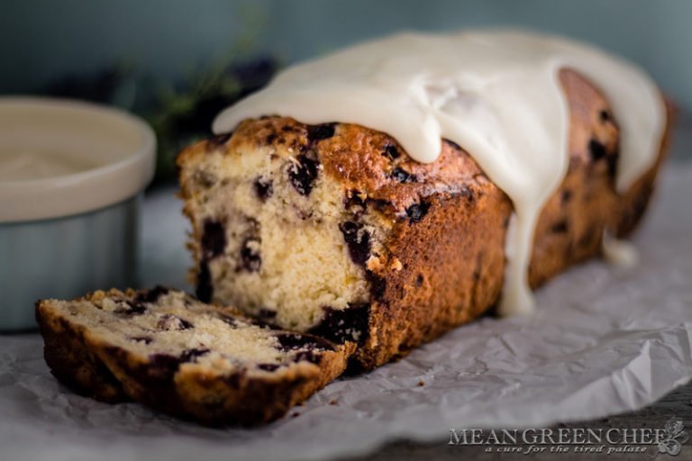 Side photo of Rustic Blueberry Banana Bread with a lush vanilla glaze dripping down a freshly sliced loaf. Mean Green Chef