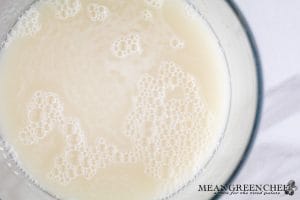 Process photo for making Soft Pretzels, of yeast blooming in warm water, in a glass bowl. Situated against a white marble counter top.