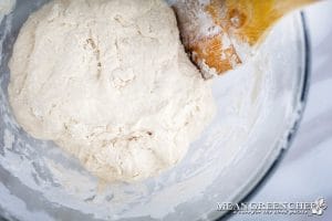 Process photo for making Soft Pretzels, flour being slowly mixed into water and yeast in a glass bowl. For making pretzel dough.