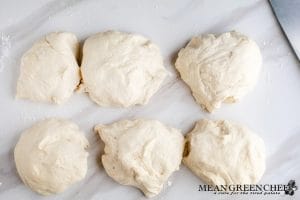 Process photo for making Soft Pretzels, the pretzel dough has been cut into individual sections. Sitting on a white marble countertop, with the glimpse of a sharp chef's knife in the upper right-hand corner of the frame.