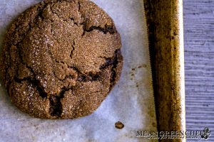 Freshly baked Best Ever Molasses Cookie close up showing crispyness of the outside of the cookie. Cooling on a piece of parchment paper on a baking sheet.