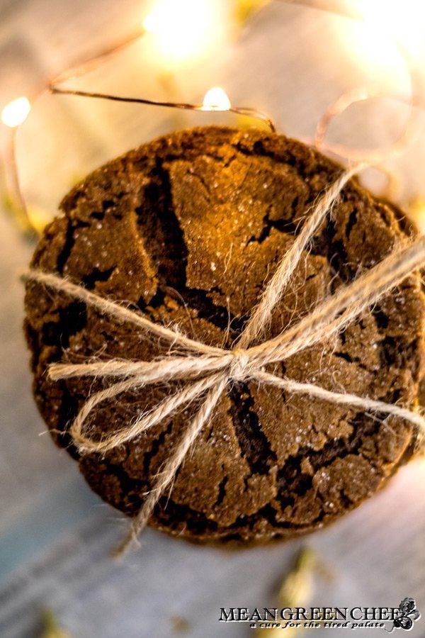 Overhead photo of a stack of Molasses Cookies, tied with twine and sitting on newspaper that has been scattered with white flower buds.