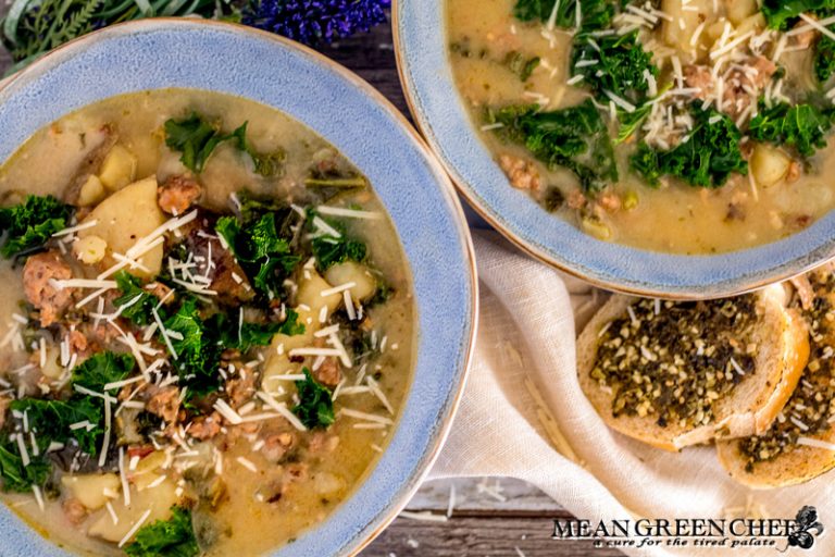 Overhead photo of Zuppa Toscana in two large blue bowls with rough edges. A small beige linen napkin and bread spread with pesto. Mean Green Chef