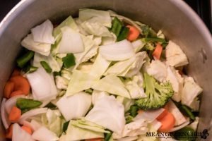 Overhead photo of Robust Cabbage Soup in two crocks one yellow one green with oregano on an old blue wooden background.