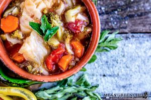 Overhead photo of Robust Cabbage Soup in two crocks one yellow one green with oregano on an old blue wooden background.