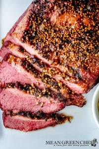 Close-up of a succulent, Guinness-Braised Corned Beef with a peppercorn crust, sliced and displayed on a white plate.