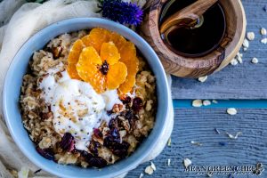 Overhead shot of a bowl of Spiced Mandarin Pecan Oatmeal garnished with whipped cream and Sumo Citrus.