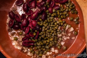 Kalamata olives and capers being added to the saucepan for Pescatore.