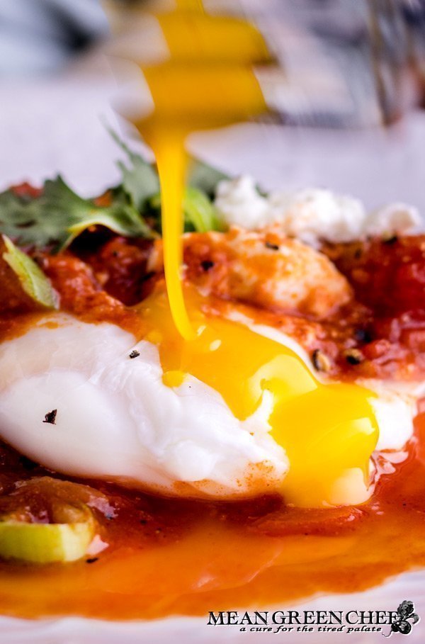 Shakshuka egg yolk being broken with a fork.