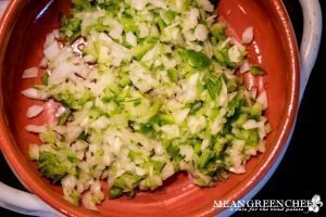 Diced onions and peppers cooking in an Italian terracotta pot for Shakshuka.