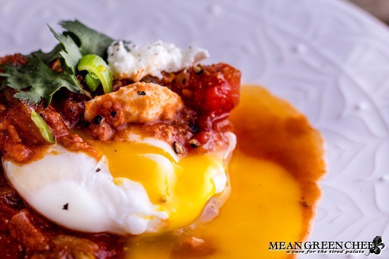 Close up of Shakshuka with broken egg yolk on a white plate.