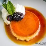 Classic Flan on a white plate with blackberries, whipped cream, and mint.