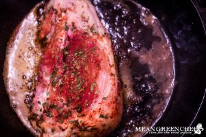 Blackened chicken cooking breast side down in a hot cast iron pan.