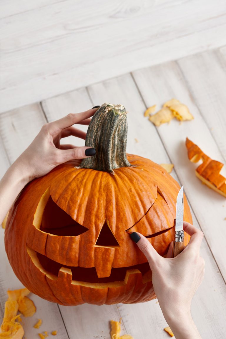 Carving Pumpkin with face being carved on white wooden background.