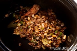 Sautéed ingredients for making Slow Cooker Texas Pinto Beans situated inside a black slow cooker crock.