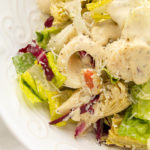 Close up of Big Easy Italian Salad in a white bowl garnished with fresh parmesan cheese