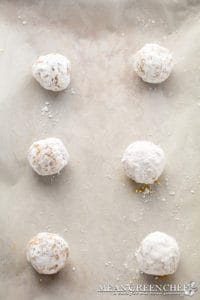 Six powdered sugar-coated Meyer Lemon Cookies, evenly spaced on a parchment paper lined sheet pan. Ready to be baked.