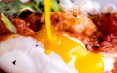 Shakshuka egg yolk being broken with a fork.