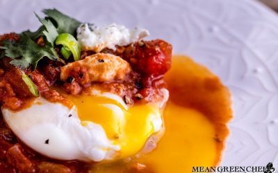 Close up of Shakshuka with broken egg yolk on a white plate.